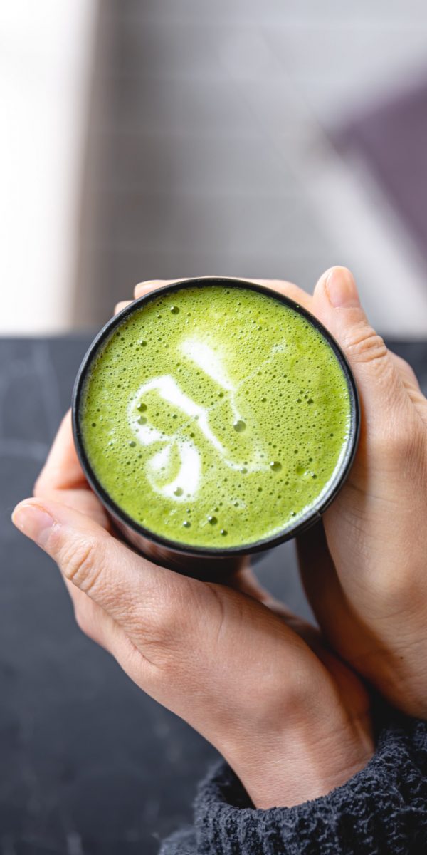 Top view of woman holding in hands trendy green matcha drink with amazing latte art in the hipster cafe.